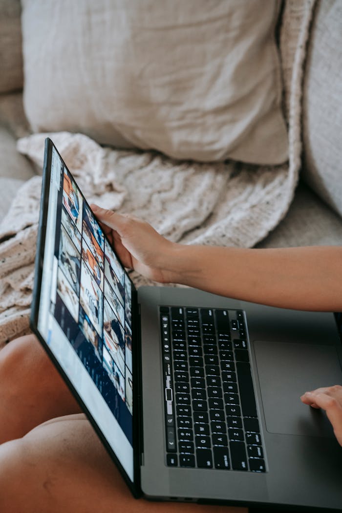 From above of crop anonymous female remote worker using laptop sitting on sofa at home